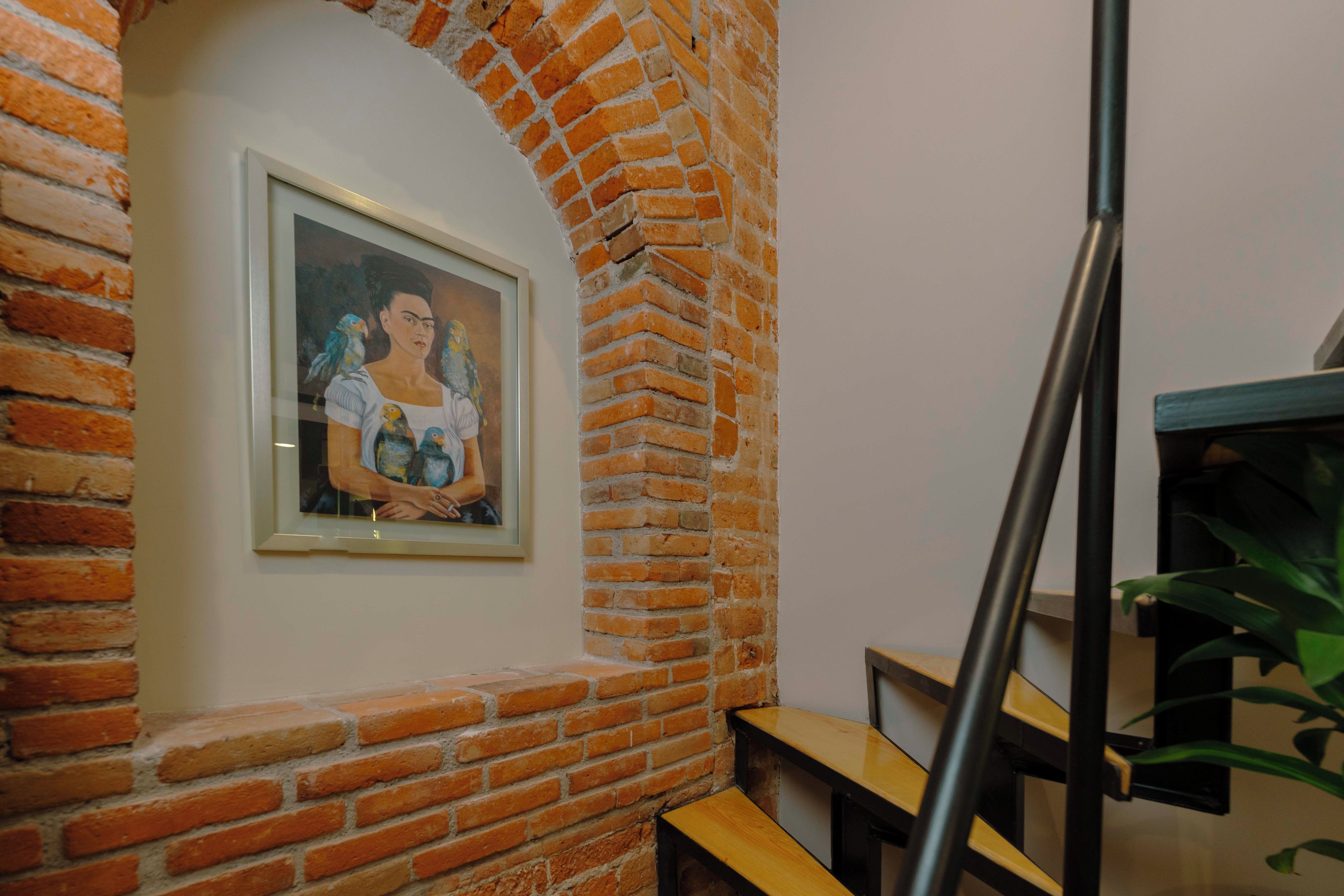 A framed artwork on a brick wall, a wooden bench, and a staircase with a metal railing.