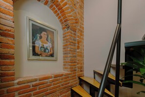Uma obra de arte emoldurada numa parede de tijolos, um banco de madeira e uma escadaria com guarda-corpo de metal.