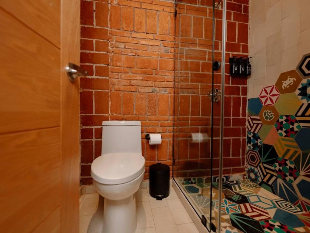 Un bagno con un WC bianco, cabina doccia in vetro e pavimento piastrellato.