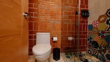 Un bagno con un WC bianco, cabina doccia in vetro e pavimento piastrellato.