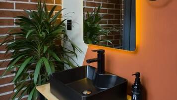 Un baño con un lavabo negro, un espejo y una planta en maceta.