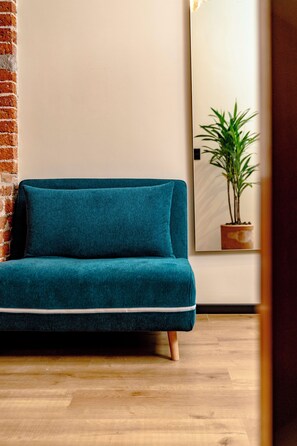 A teal sofa with a cushion, positioned against a brick wall and a wooden floor. - HOTEL TERRACOTA MX (Mexico City)