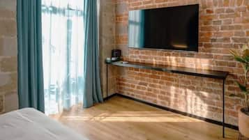Un dormitorio con pared de ladrillo, televisor montado, cama y ventana con cortinas.