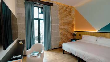 Habitación de hotel con cama, escritorio con silla, televisión y ventana con cortinas.