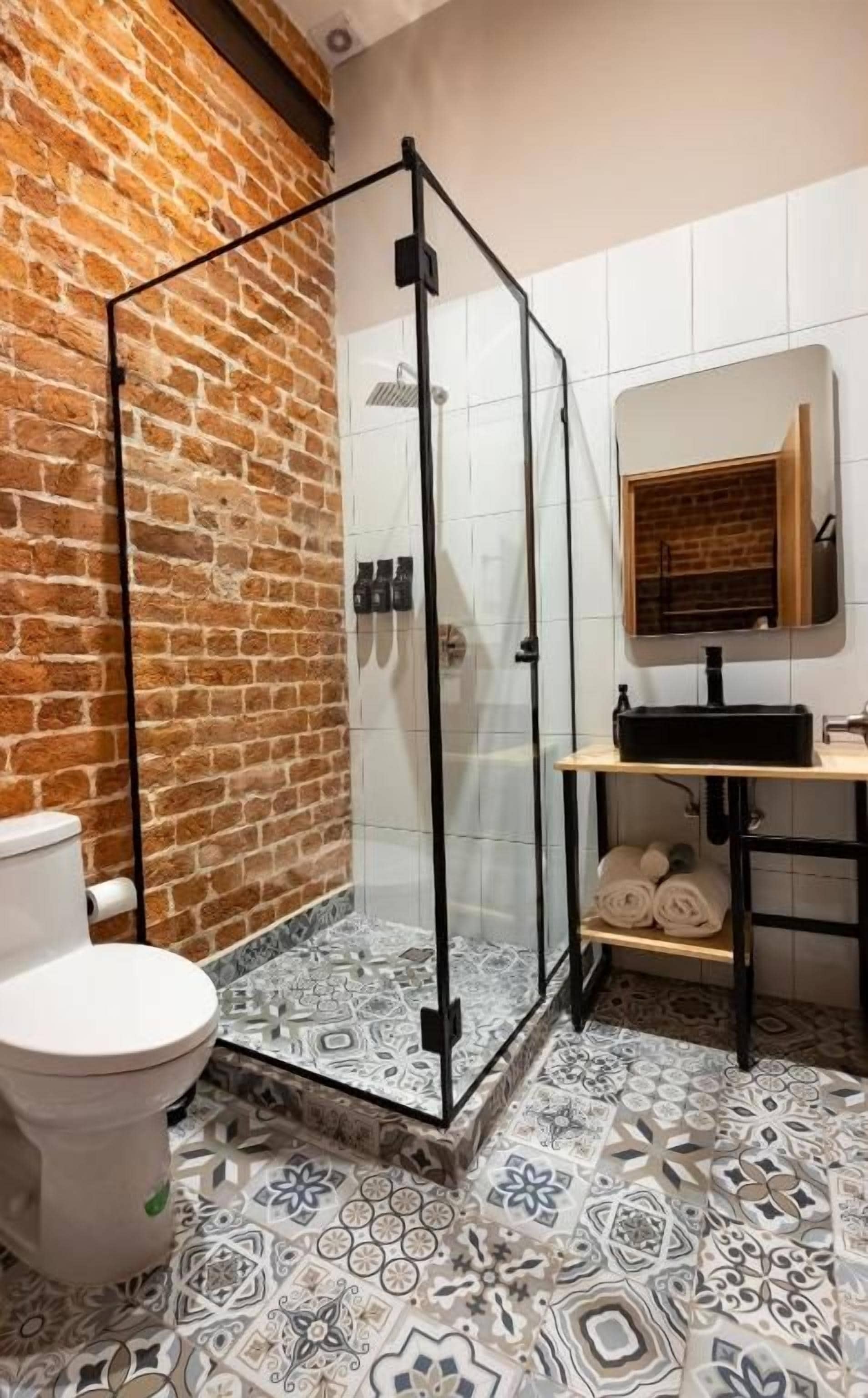 Un bagno con box doccia in vetro, un water, piastrelle a motivi decorativi e uno scaffale in legno con asciugamani.