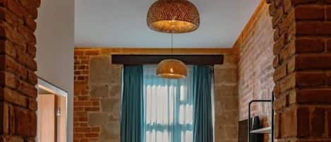 A narrow hallway with a brick archway, a bed, a hanging light fixture, and a potted plant.