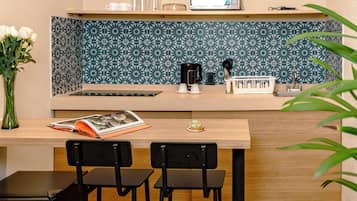 Una cocina compacta con cubierta de madera, dos sillas negras, una mesita y electrodomésticos como microondas y cafetera.