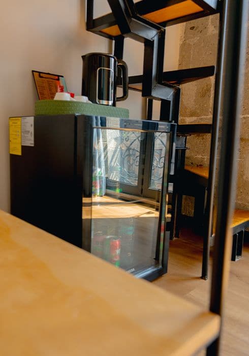 A room with a wooden table, a black refrigerator, and a glass door leading to a kitchen area.