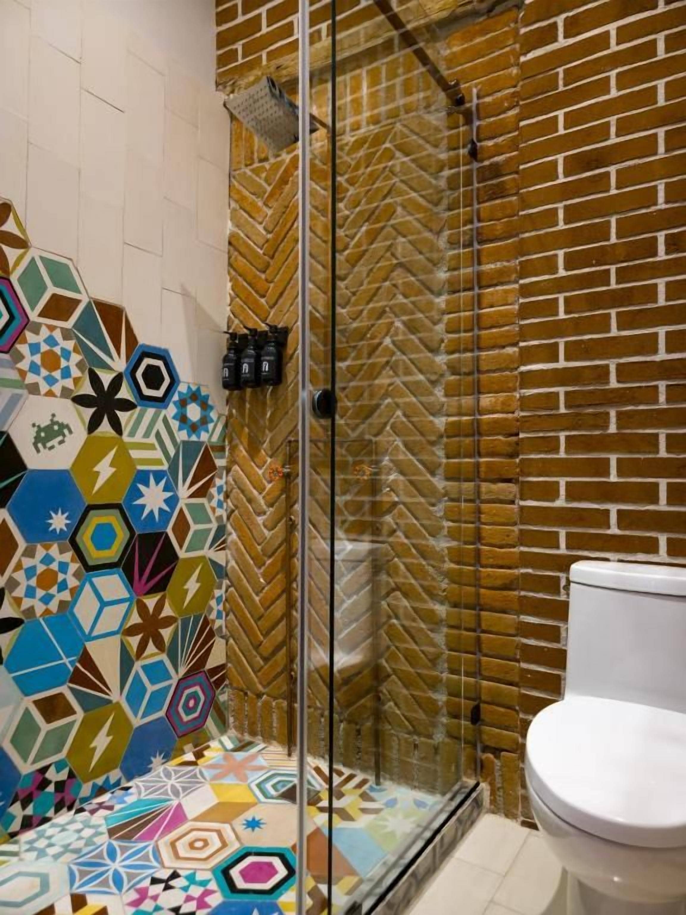 Un bagno con doccia, WC e parete rivestita di piastrelle esagonali colorate.