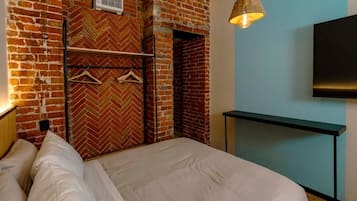 Una camera d'albergo con una parete in mattoni, un letto con biancheria bianca, un lampadario e un televisore a schermo piatto fissato al muro.