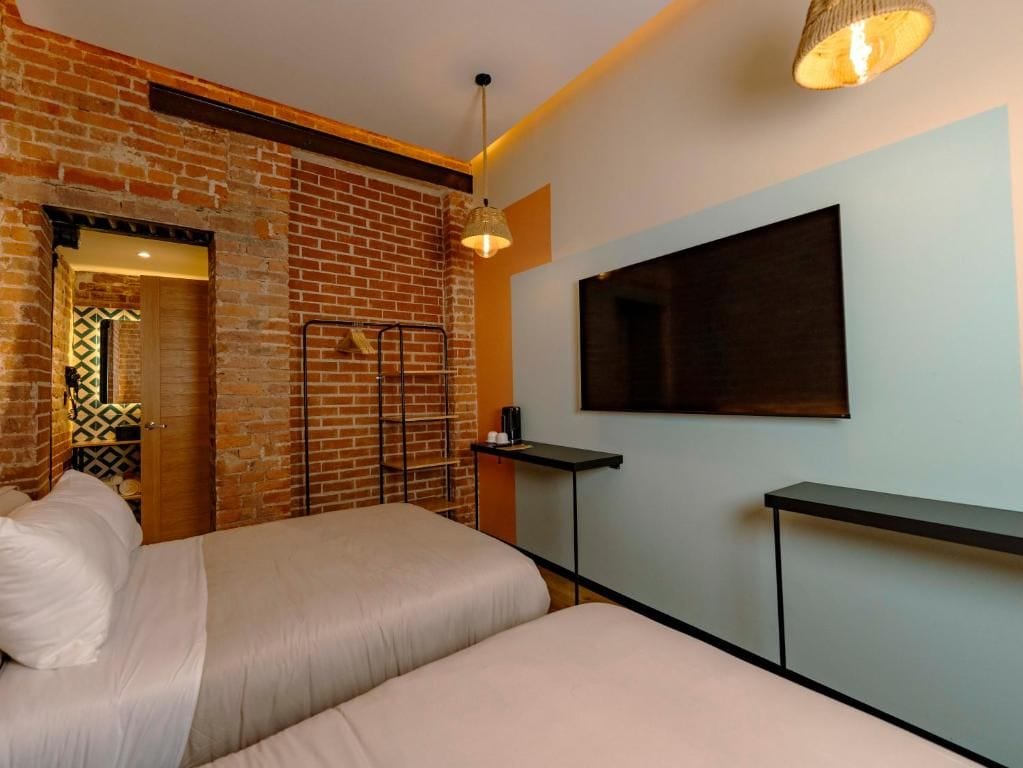 Habitación de hotel con pared de ladrillo, una cama, un televisor montado y una mesita.