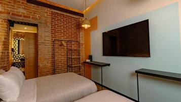 Habitación de hotel con pared de ladrillo, una cama, un televisor montado y una mesita.