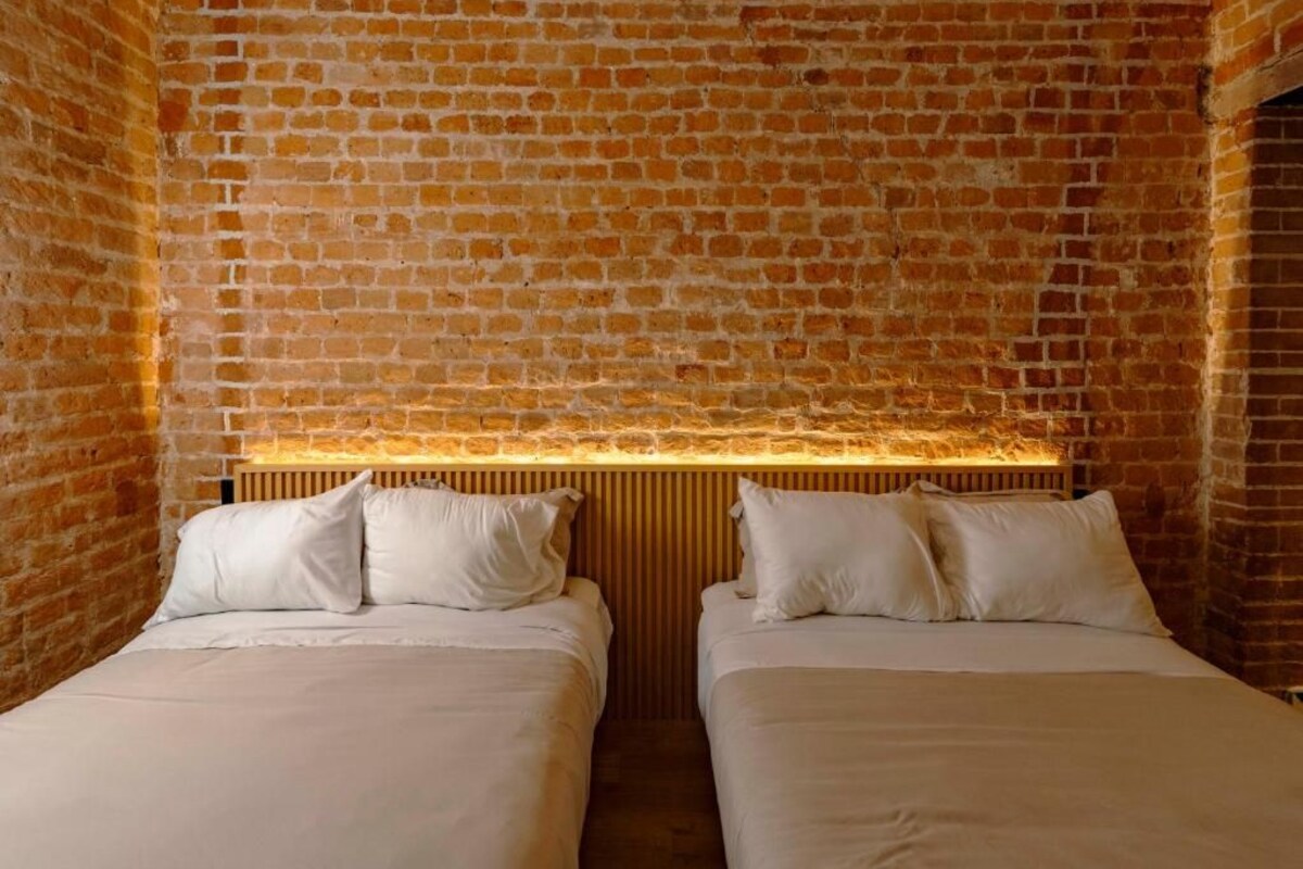 A room with two beds, a brick wall, and a wooden headboard.