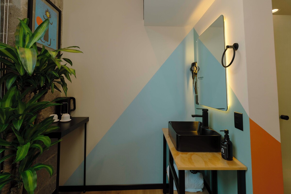 A modern bathroom with a black sink, a mirror with integrated lighting, a towel rack, and a potted plant.