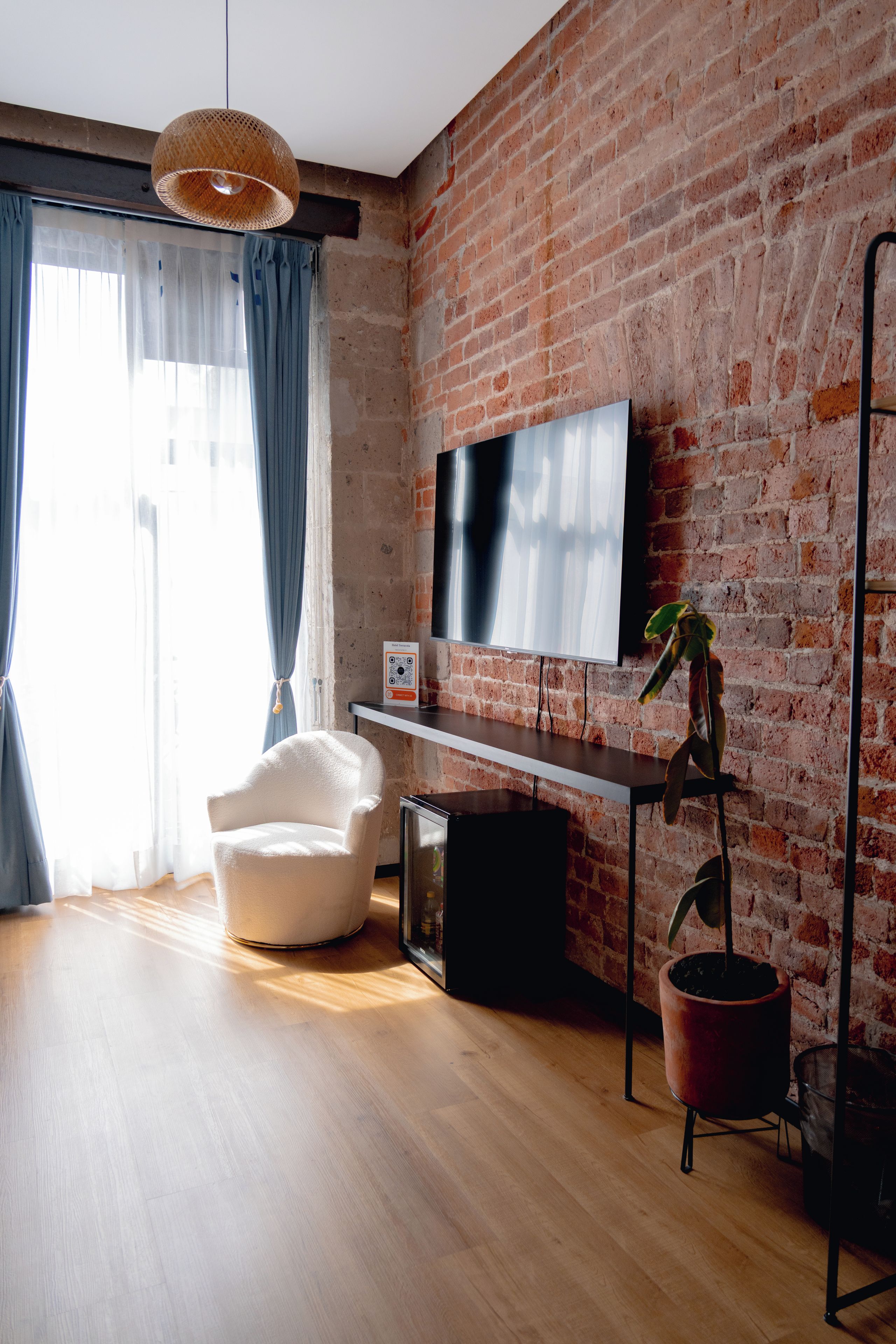 Una sala de estar moderna con pared de ladrillo, un televisor de pantalla plana montado en la pared, un sillón blanco, piso de madera y una lámpara colgante.