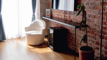 Una sala de estar moderna con pared de ladrillo, un televisor de pantalla plana montado en la pared, un sillón blanco, piso de madera y una lámpara colgante.