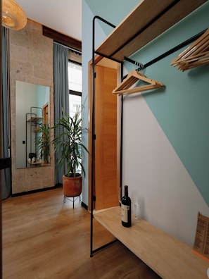 Un interior moderno con piso de madera, un espejo grande, una planta en maceta, una botella de vino y una percha.