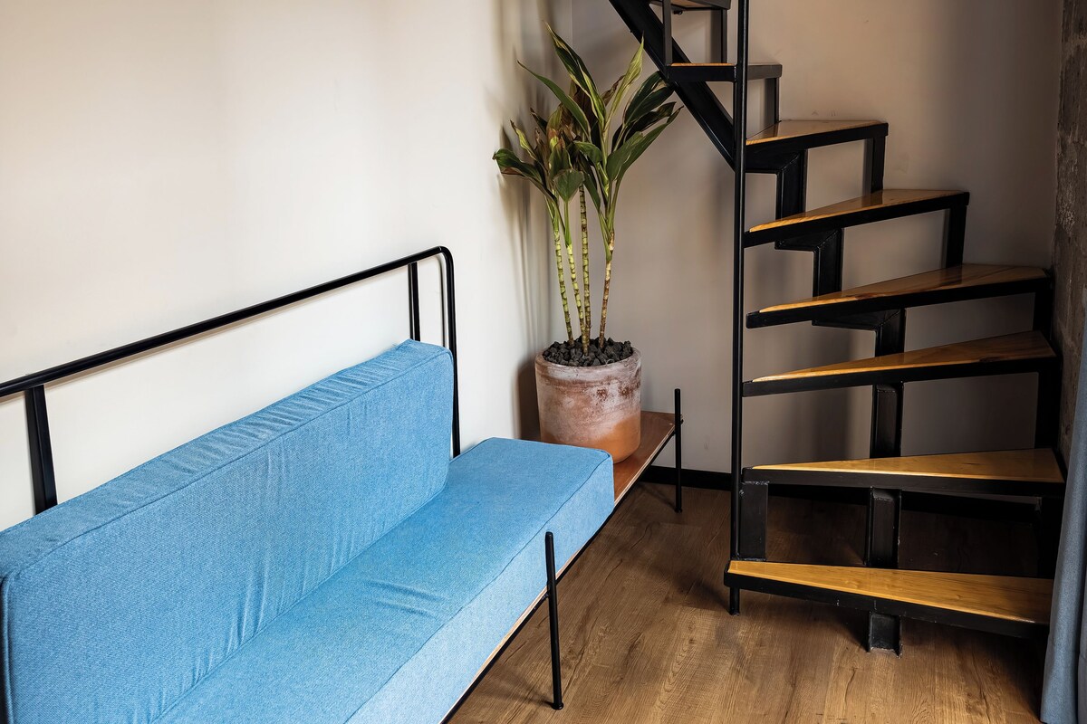 A modern interior with a blue sofa, a wooden staircase, and a potted plant.