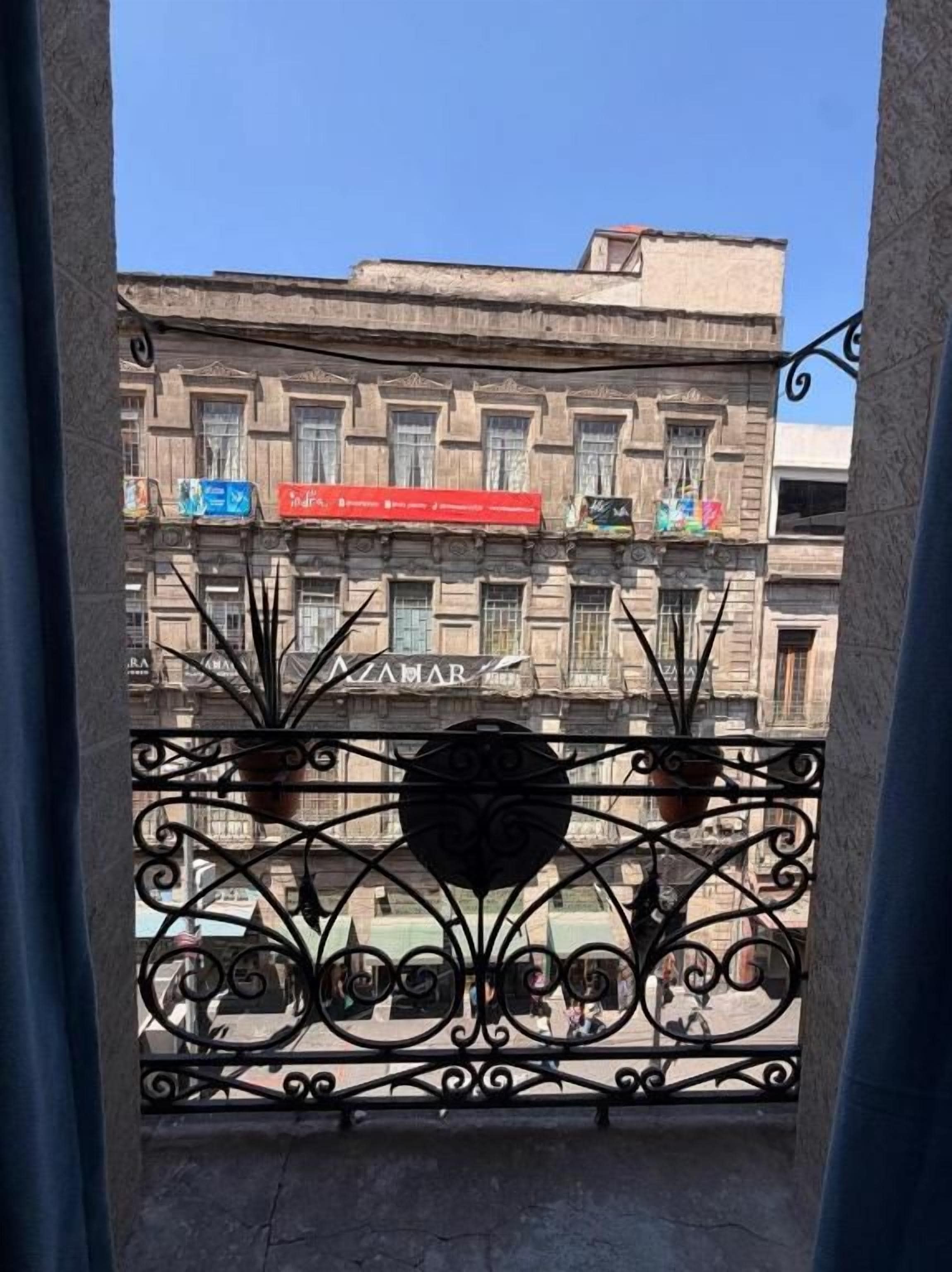 Un balcón con barandillas de hierro forjado decoradas y vistas a un edificio con varios balcones y letreros.