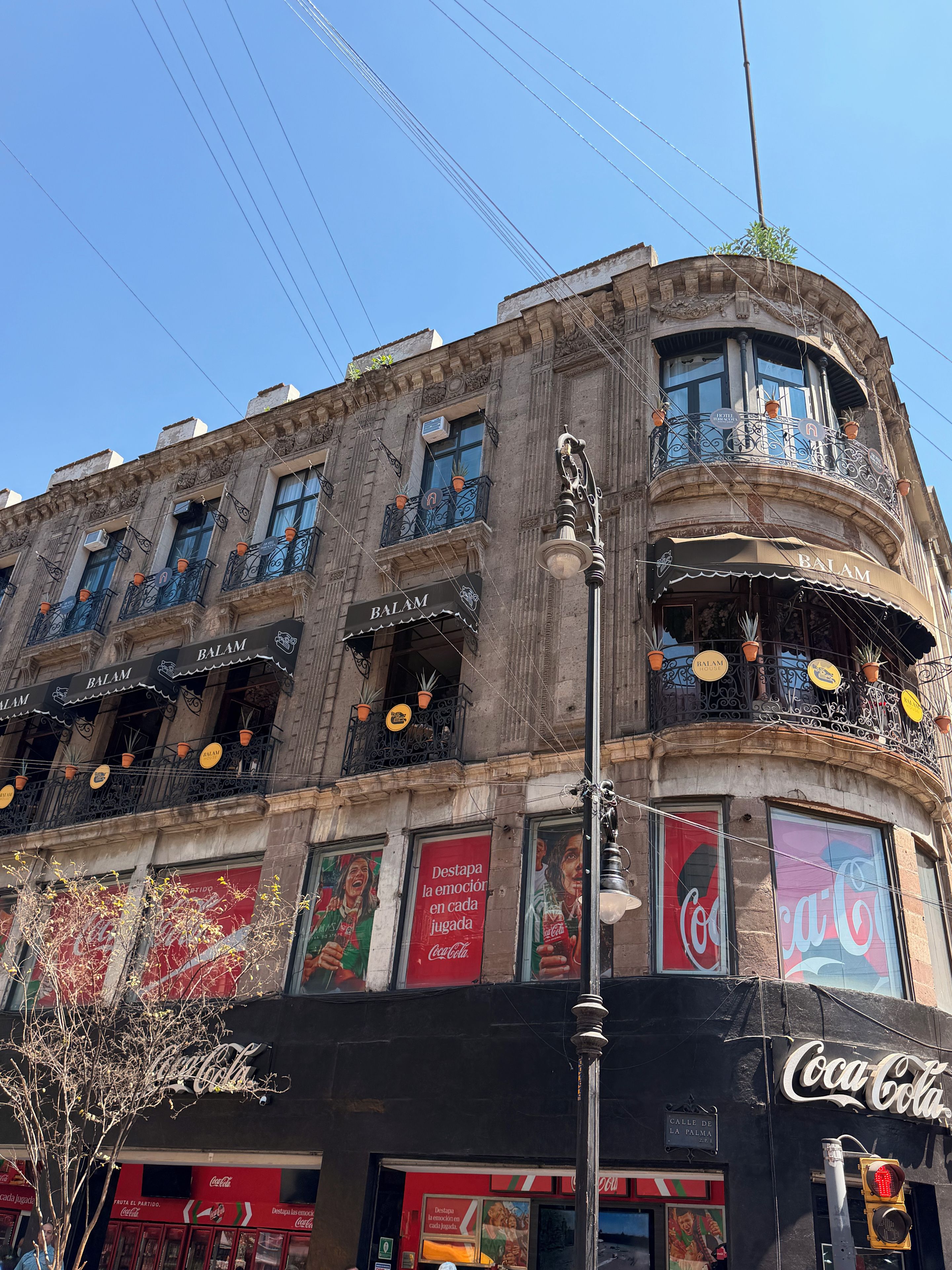 A building with multiple balconies, some with potted plants, and storefronts with Coca-Cola branding.