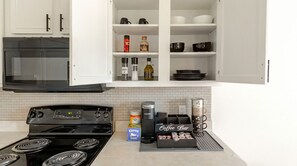 A kitchen with a stove, oven, and various appliances. There are cabinets above the counter and a coffee bar setup on the counter.