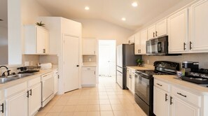 Una cocina con armarios blancos, electrodomésticos de acero inoxidable y piso de baldosas.