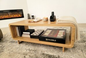 A wooden coffee table with a Scrabble box, books, a candle, and a remote control.