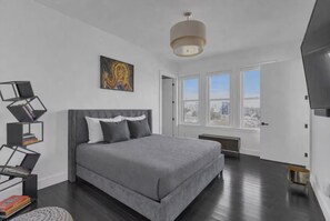 A modern bedroom with a large bed, a unique bookshelf, and a city view through the windows. - Lovely XL Rare Penthouse, Master Spa Bedroom, 3 Balconies & More (Atlanta)