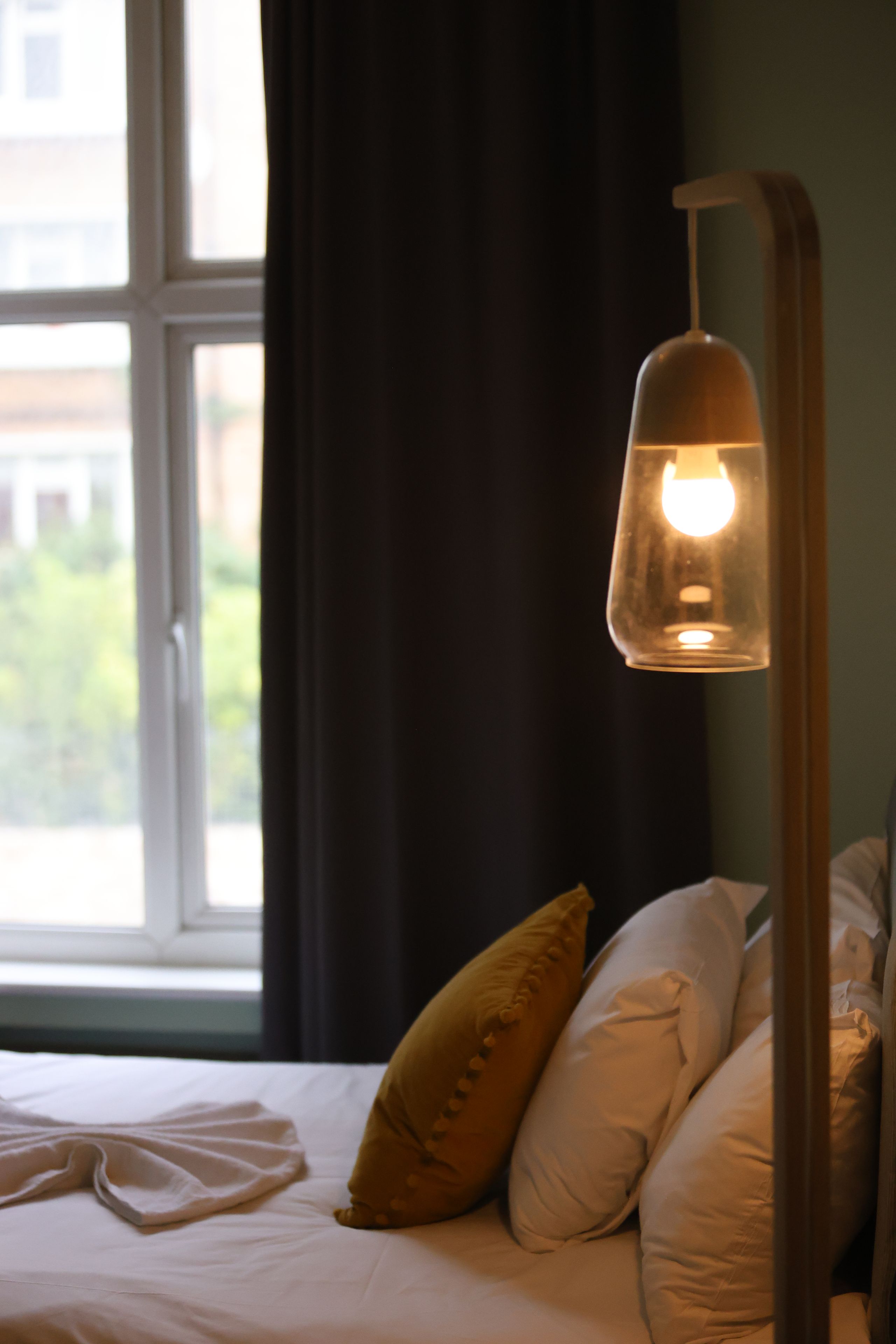 A bed with white bedding and two pillows, a window with curtains, and a hanging lamp.