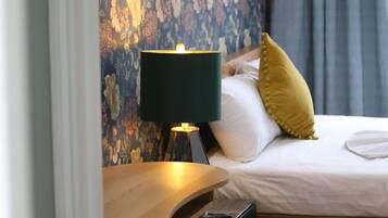 A hotel room with a bed, a desk, a lamp, and a floral wallpaper.