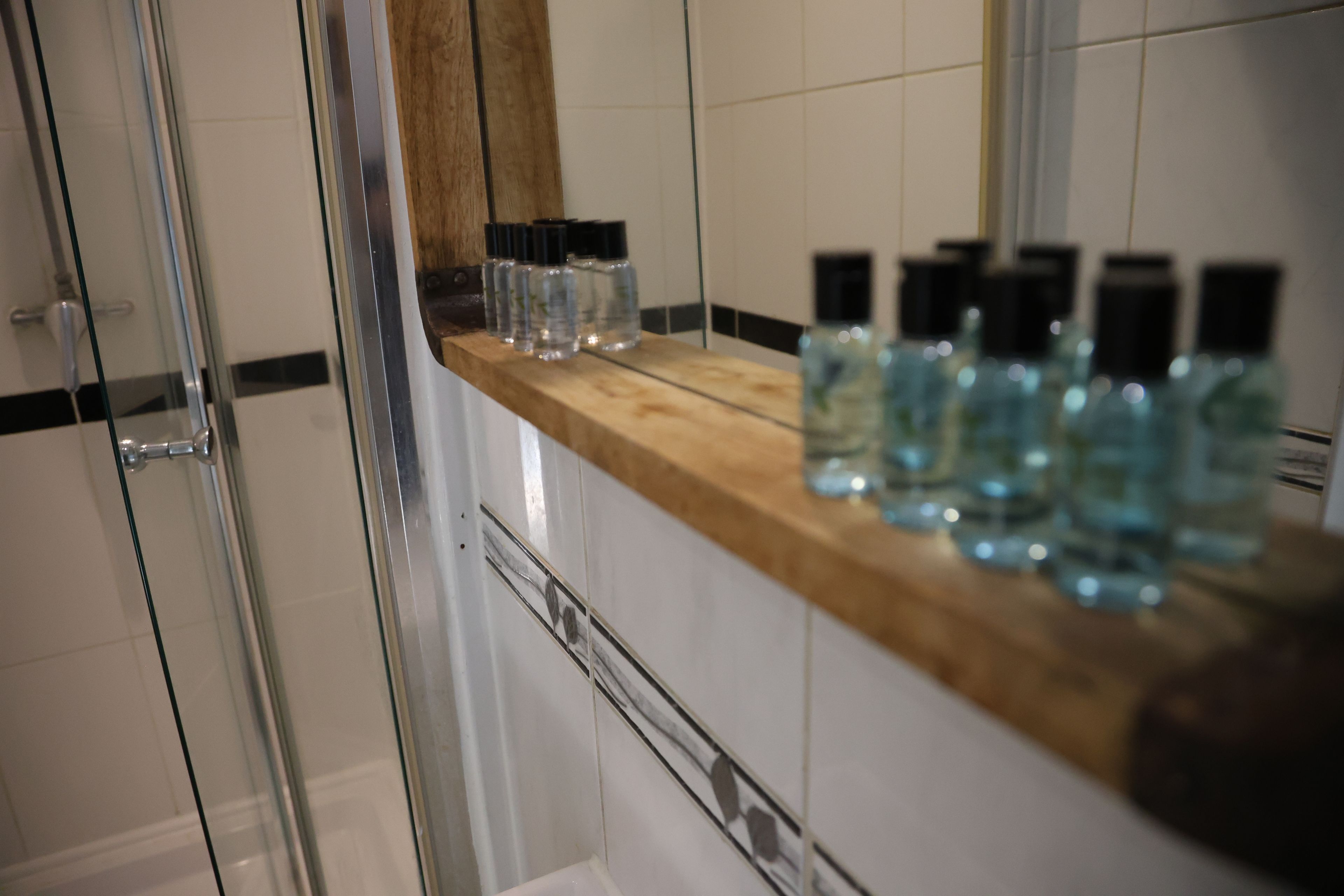 A bathroom with a glass shower enclosure, a wooden countertop, and several bottles of liquid.