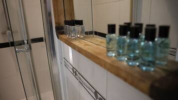 A bathroom with a glass shower enclosure, a wooden countertop, and several bottles of liquid.