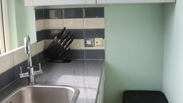 A kitchen with a stainless steel sink, a knife block, and a trash bin.