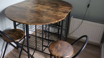 A round wooden table with metal legs and two wooden chairs, positioned in a room with a window and a radiator.