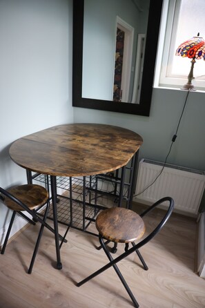A round wooden table with metal legs and two wooden chairs, positioned in a room with a window and a radiator. - The Good Vibe (London)