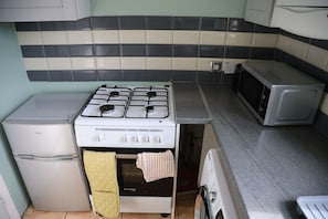 Cozinha com fogão branco, micro-ondas e pequena geladeira.