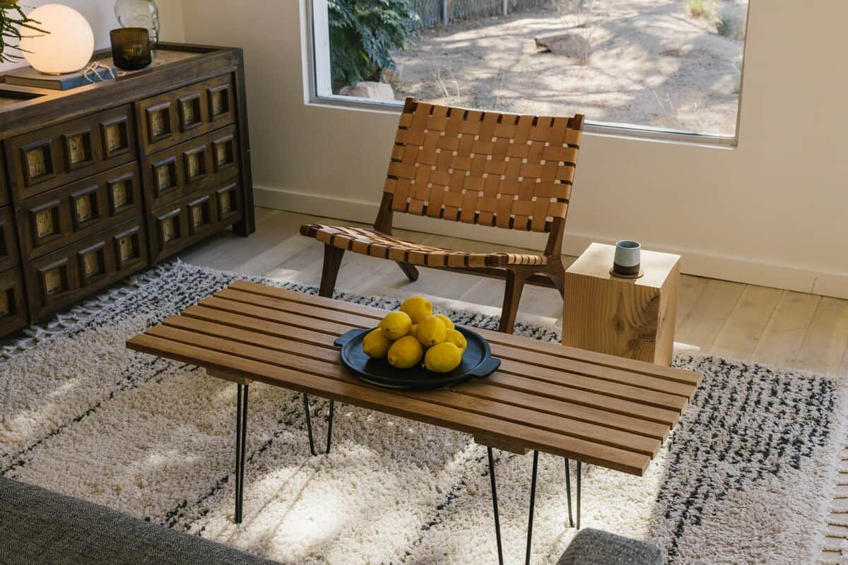 Une chaise en bois avec un dossier en osier, une table en bois sur laquelle se trouve une assiette de citrons, et une petite table d’appoint en bois avec une tasse.