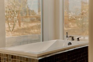 Ein Badezimmer mit einem großen Fenster, einem Waschbecken mit Wasserhahn und Fliesenwänden.