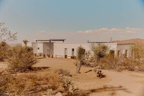 A single-story building with a flat roof, surrounded by desert vegetation. - Quail Springs Ranch | Pool & Spa (Joshua Tree)