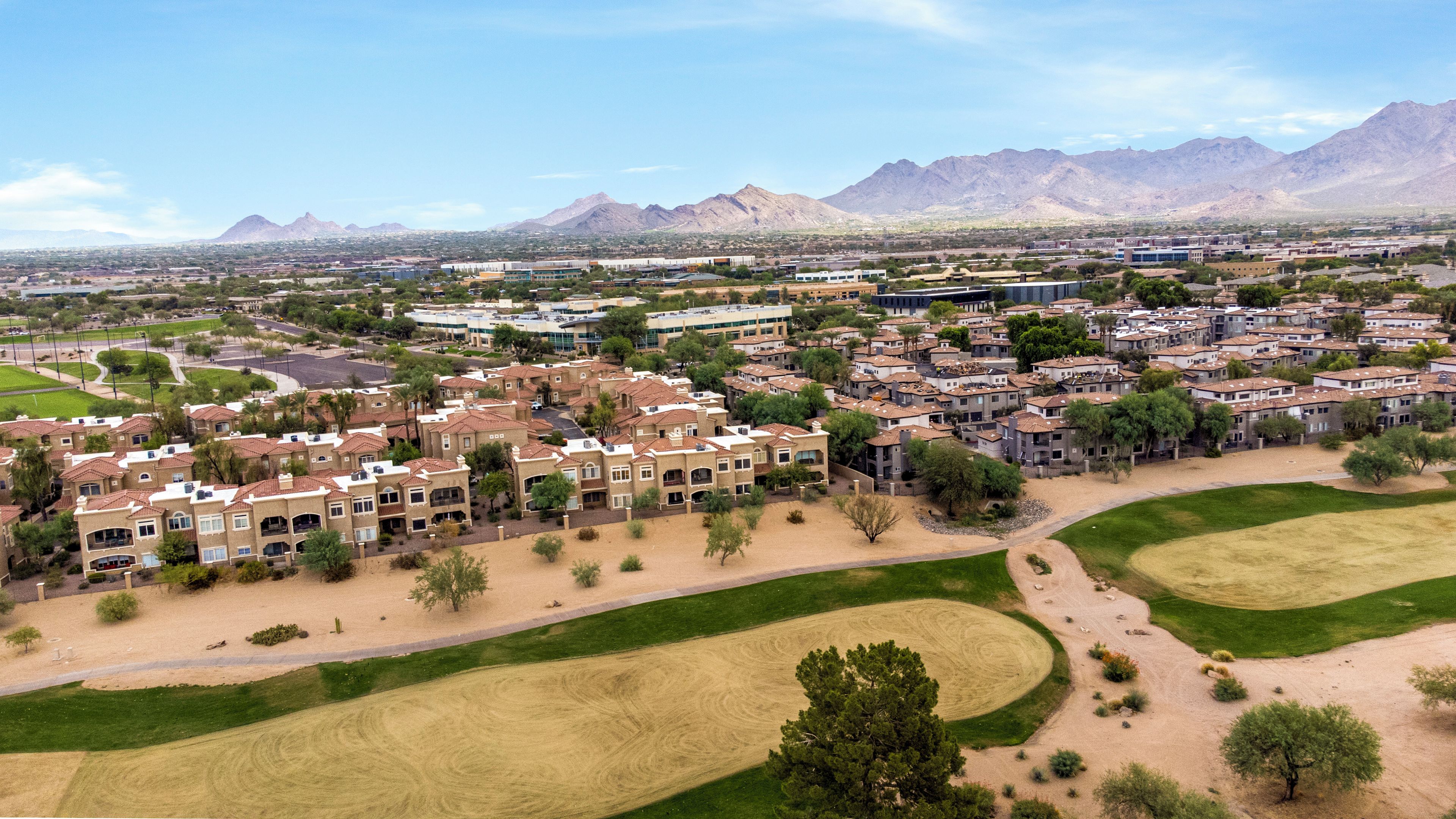 Vista aérea de una zona residencial con varios edificios, espacios verdes y montañas al fondo.