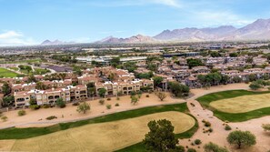 Vista aérea de una zona residencial con varios edificios, espacios verdes y montañas al fondo.