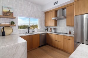 Una cocina moderna con armarios de madera, un refrigerador de acero inoxidable y una ventana con vistas a árboles.