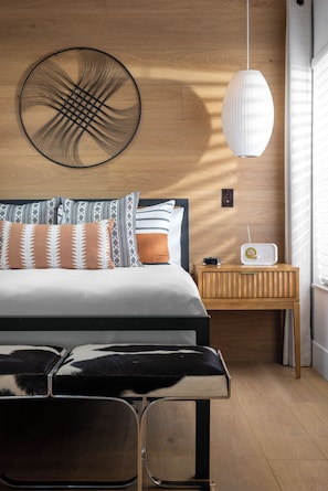 A modern bedroom with a wooden headboard, a large bed with patterned pillows, a bedside table with a radio, and a wall-mounted light fixture. - The Fairway House Scottsdale (Scottsdale)