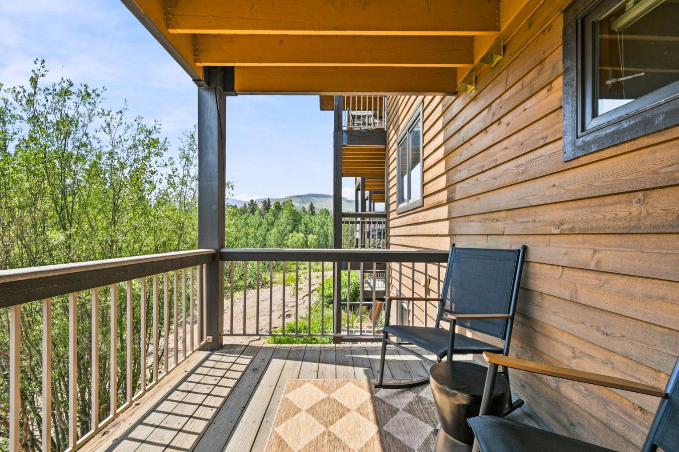 A wooden balcony with a metal railing, a chair, and a small table.
