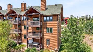 A multi-story wooden building with balconies, a visible outdoor area, and a forested background.