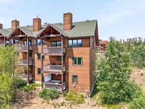 A multi-story wooden building with balconies, a visible outdoor area, and a forested background.