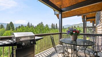 A balcony with a grill, outdoor table, chairs, and a potted plant.