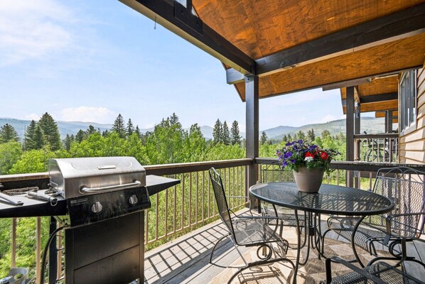 A balcony with a grill, outdoor table, chairs, and a potted plant.