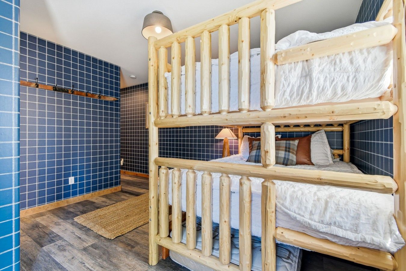 A bunk bed with a wooden frame, a blue tiled wall, and a wooden floor.