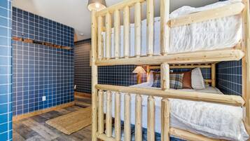 A bunk bed with a wooden frame, a blue tiled wall, and a wooden floor.